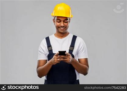 profession, construction and building - happy smiling indian worker or builder in helmet using smartphone over grey background. happy indian or builder in helmet using smartphone