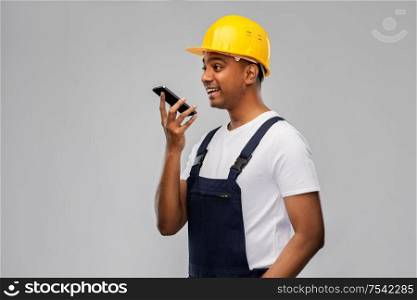 profession, construction and building - happy smiling indian worker or builder in helmet using voice command recorder on smartphone over grey background. happy indian builder recording voice on smartphone