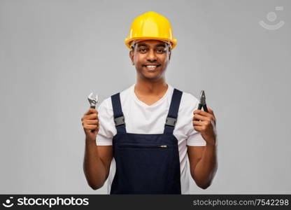 profession, construction and building - happy smiling indian worker or builder in helmet with wrench and pliers over grey background. indian builder in helmet with wrench and pliers