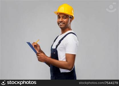 profession, construction and building - happy smiling indian worker or builder in helmet with clipboard and pencil over grey background. happy builder in helmet with clipboard and pencil