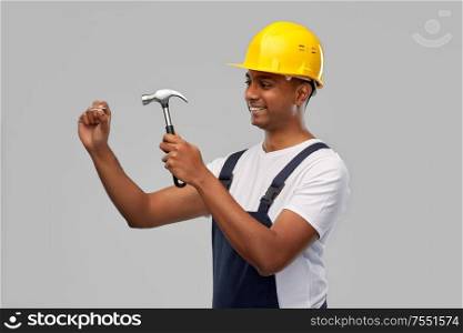 profession, construction and building - happy smiling indian worker or builder in helmet with hammer and nail over grey background. happy indian worker or builder hammering nail