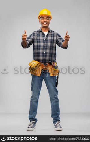 profession, construction and building - happy smiling indian worker or builder in helmet showing thumbs up over grey background. happy indian worker or builder showing thumbs up