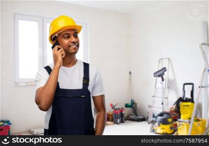 profession, construction and building - happy smiling indian worker or builder in helmet calling on smartphone over room with working equipment at new home or apartment background. indian builder in helmet calling on smartphone