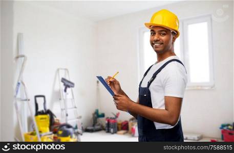 profession, construction and building - happy smiling indian worker or builder in helmet with clipboard and pencil over room with working equipment at new home or apartment background. happy builder in helmet with clipboard and pencil