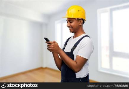 profession, construction and building - happy smiling indian worker or builder in helmet using smartphone over empty room at new home or apartment background. happy indian or builder in helmet using smartphone