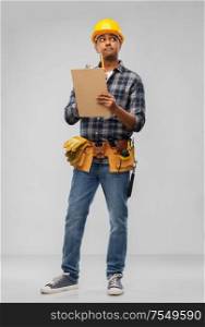 profession, construction and building - thinking indian worker or builder in helmet with clipboard and pencil over grey background. thinking builder with clipboard and pencil