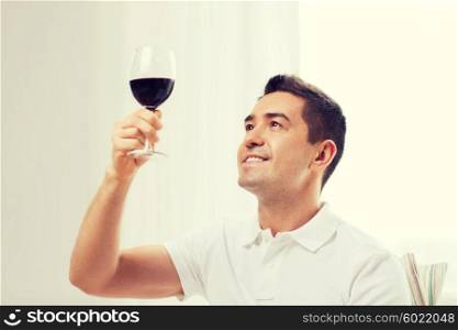 profession, drinks, leisure and people concept - happy man drinking red wine from glass at home