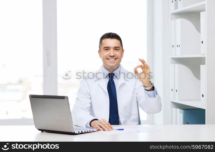 profession, gesture, people, technology and medicine concept - smiling male doctor in white coat with laptop pomputer showing ok in medical office