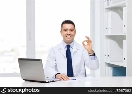 profession, gesture, people, technology and medicine concept - smiling male doctor in white coat with laptop pomputer showing ok in medical office