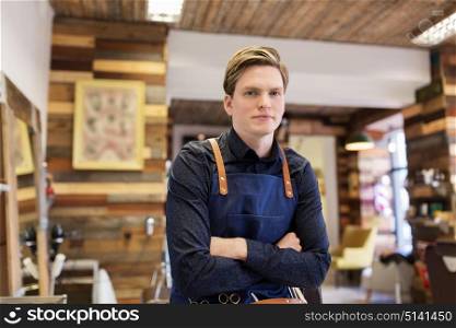 profession, grooming and people concept - male stylist or hairdresser in apron at hair salon or barbershop. male hairdresser at hair salon or barbershop