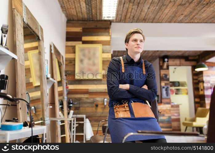 profession, grooming and people concept - male stylist or hairdresser with scissors in apron at hair salon or barbershop. male hairdresser at hair salon or barbershop