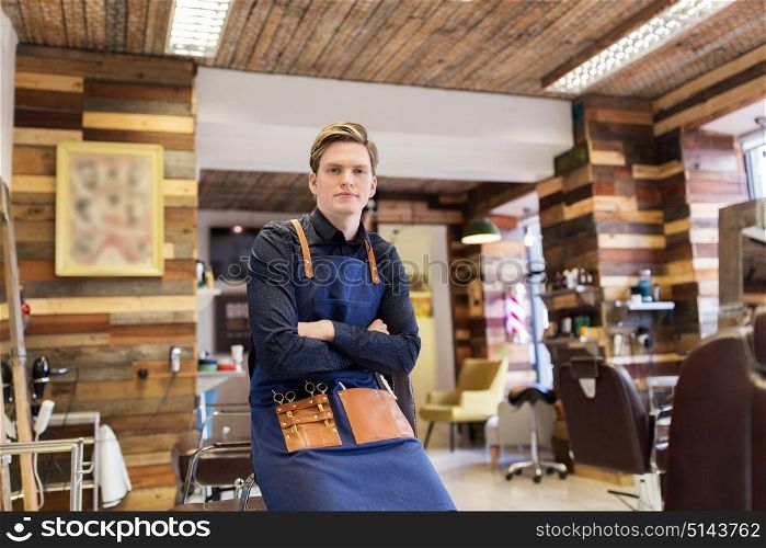 profession, grooming and people concept - male stylist or hairdresser with scissors in apron at hair salon or barbershop. male hairdresser at hair salon or barbershop
