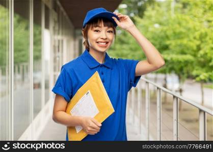 profession, job and people concept - happy smiling delivery woman or postwoman in blue uniform holding parcel envelope over city street background. happy delivery woman holding parcel envelope