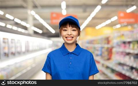 profession, job and people concept - happy smiling delivery woman or saleswoman in blue uniform over supermarket background. happy delivery woman or saleswoman at supermarket