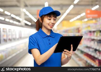 profession, job and people concept - happy smiling delivery woman or saleswoman in blue uniform with tablet pc computer over supermarket background. happy smiling delivery woman with tablet computer