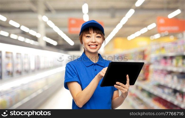 profession, job and people concept - happy smiling delivery woman or saleswoman in blue uniform with tablet pc computer over supermarket background. happy smiling delivery woman with tablet computer