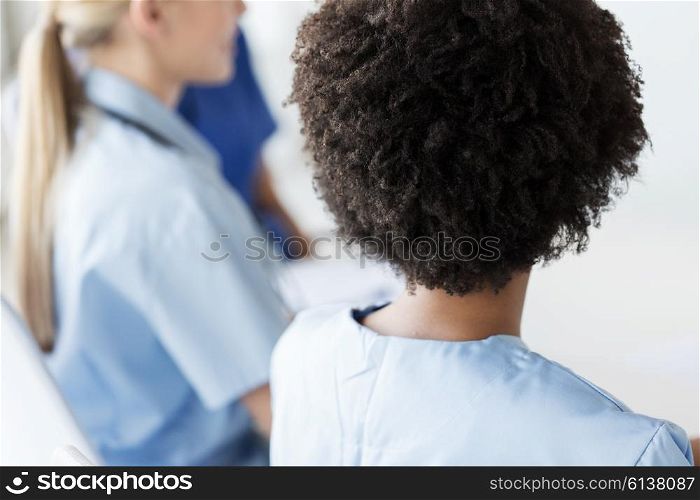 profession, people and medicine concept - close up of african female doctor or nurse with group of medics at conference in hospital from back