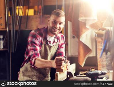 profession, people, carpentry, woodwork and people concept - happy carpenter with jointer planing wood plank at workshop. carpenter working with plane and wood at workshop. carpenter working with plane and wood at workshop