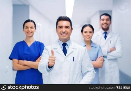 profession, people, health care, gesture and medicine concept - group of happy medics or doctors at hospital corridor showing thumbs up. medics or doctors at hospital showing thumbs up