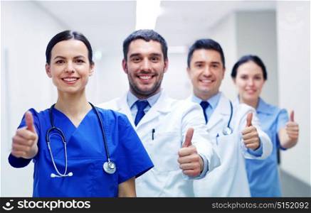 profession, people, health care, gesture and medicine concept - group of happy medics or doctors at hospital corridor showing thumbs up. medics or doctors at hospital showing thumbs up