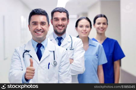 profession, people, health care, gesture and medicine concept - group of happy medics or doctors at hospital corridor showing thumbs up. medics or doctors at hospital showing thumbs up