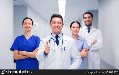 profession, people, health care, gesture and medicine concept - group of happy medics or doctors at hospital corridor showing thumbs up. medics or doctors at hospital showing thumbs up