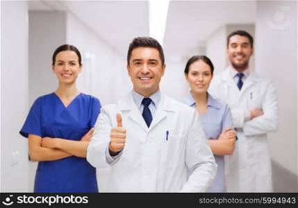 profession, people, health care, gesture and medicine concept - group of happy medics or doctors at hospital corridor showing thumbs up