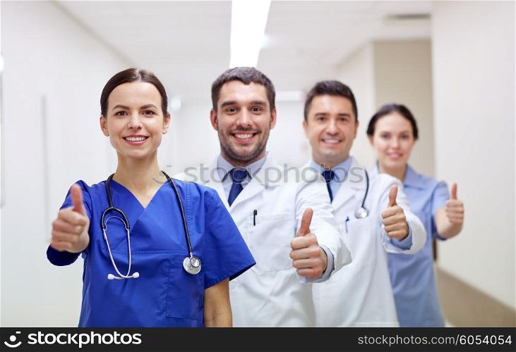 profession, people, health care, gesture and medicine concept - group of happy medics or doctors at hospital corridor showing thumbs up