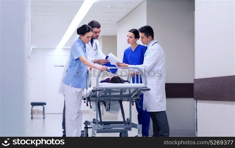 profession, people, health care, reanimation and medicine concept - group of medics or doctors carrying unconscious woman patient on hospital gurney to emergency. medics with woman on hospital gurney at emergency