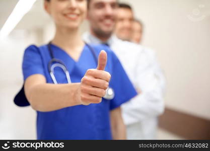 profession, people, healthcare, gesture and medicine concept - close up of happy medics or doctors at hospital corridor showing thumbs up