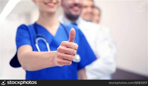 profession, people, healthcare, gesture and medicine concept - close up of happy medics or doctors at hospital corridor showing thumbs up. close up of doctors at hospital showing thumbs