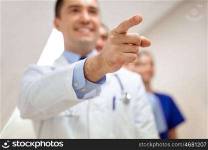 profession, people, healthcare, medicare and medicine concept - close up of happy medics or doctors pointing finger at hospital corridor