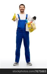 profession, service and people - happy smiling male worker or cleaner in overal and gloves with cleaning supplies showing thumbs up over white background. cleaner with cleaning supplies showing thumbs up