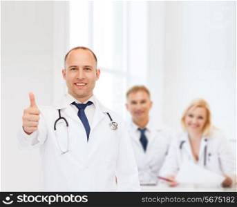 profession, teamwork, gesture and medicine concept - smiling male doctor with stethoscope in coat over group of medics showing thumbs up