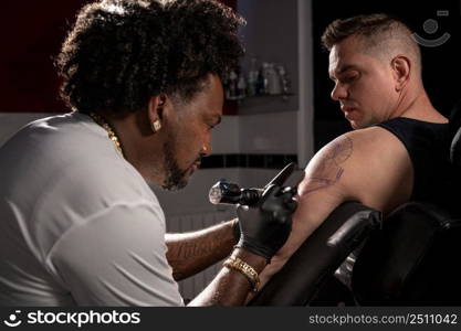 Professional African American tattoo artist makes a tattoo on client arm. High quality photography.. Professional African American tattoo artist makes a tattoo on client arm