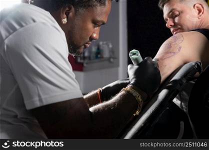 Professional African American tattoo artist makes a tattoo on client arm. High quality photography.. Professional African American tattoo artist makes a tattoo on client arm
