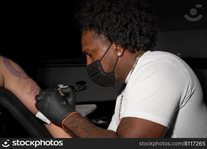 Professional African American tattoo artist makes a tattoo on client arm. High quality photography.. Professional African American tattoo artist makes a tattoo on client arm