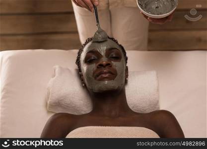 Professional applying mud mask to african woman at spa salon. Top view