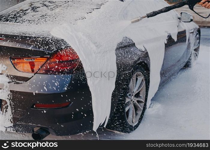 Professional auto cleaning. Exterior car wash with high pressure foam gun at self-service station, vehicle covered in soap suds during carwashing. Professional auto cleaning, car wash with high pressure foam gun