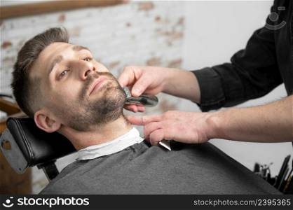 Professional barber cutting beard of handsome man. High quality photography.. Professional barber cutting beard of handsome man