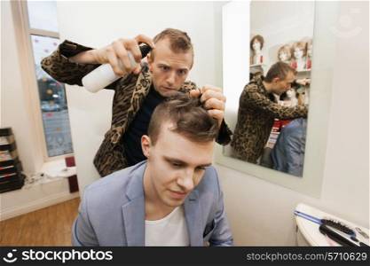 Professional barber using hairspray on male customer in shop