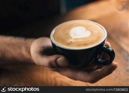 Professional barista holding black coffee cup with beautiful heart latte art surface.