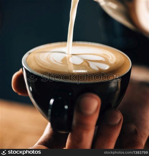 Professional barista pouring steamed milk into coffee cup making beautiful latte art Rosetta pattern.
