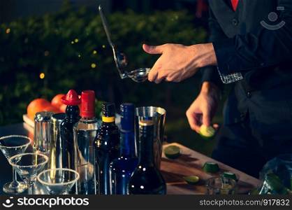 Professional bartender preparing fresh lime lemonade cocktail in drinking wine glass with ice at night bar clubbing counter. Occupation and people lifestyles concept. Outdoor background