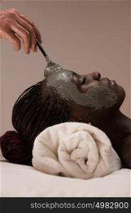 Professional beautician applying mud mask to african woman at spa salon
