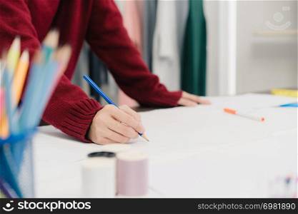Professional beautiful Asian female fashion designer working with fabric sketches and drawing clothing design at the studio. Lifestyle women working concept.
