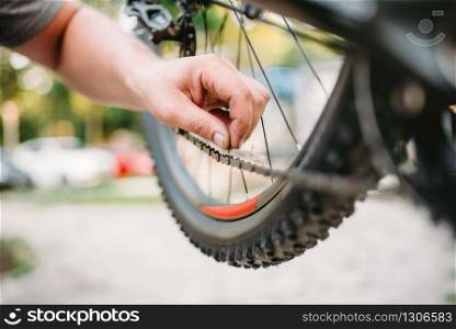 Professional bicycle mechanic in apron adjusts bike chain. Cycle workshop outdoor. Bicycling sport, bearded service man work with wheel. Bicycle mechanic in apron adjusts bike chain