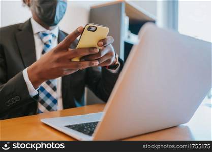 Professional businessman wearing face mask and using his mobile phone while working at office. Business concept.