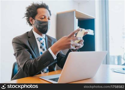 Professional businessman wearing face mask and using his mobile phone while working at office. Business concept.