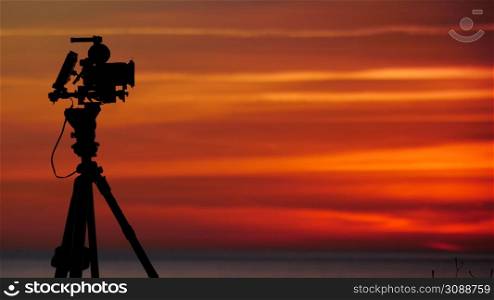 Professional camera on tripod taking picture film video of sunrise over sea.. Camera taking picture of sunrise over sea